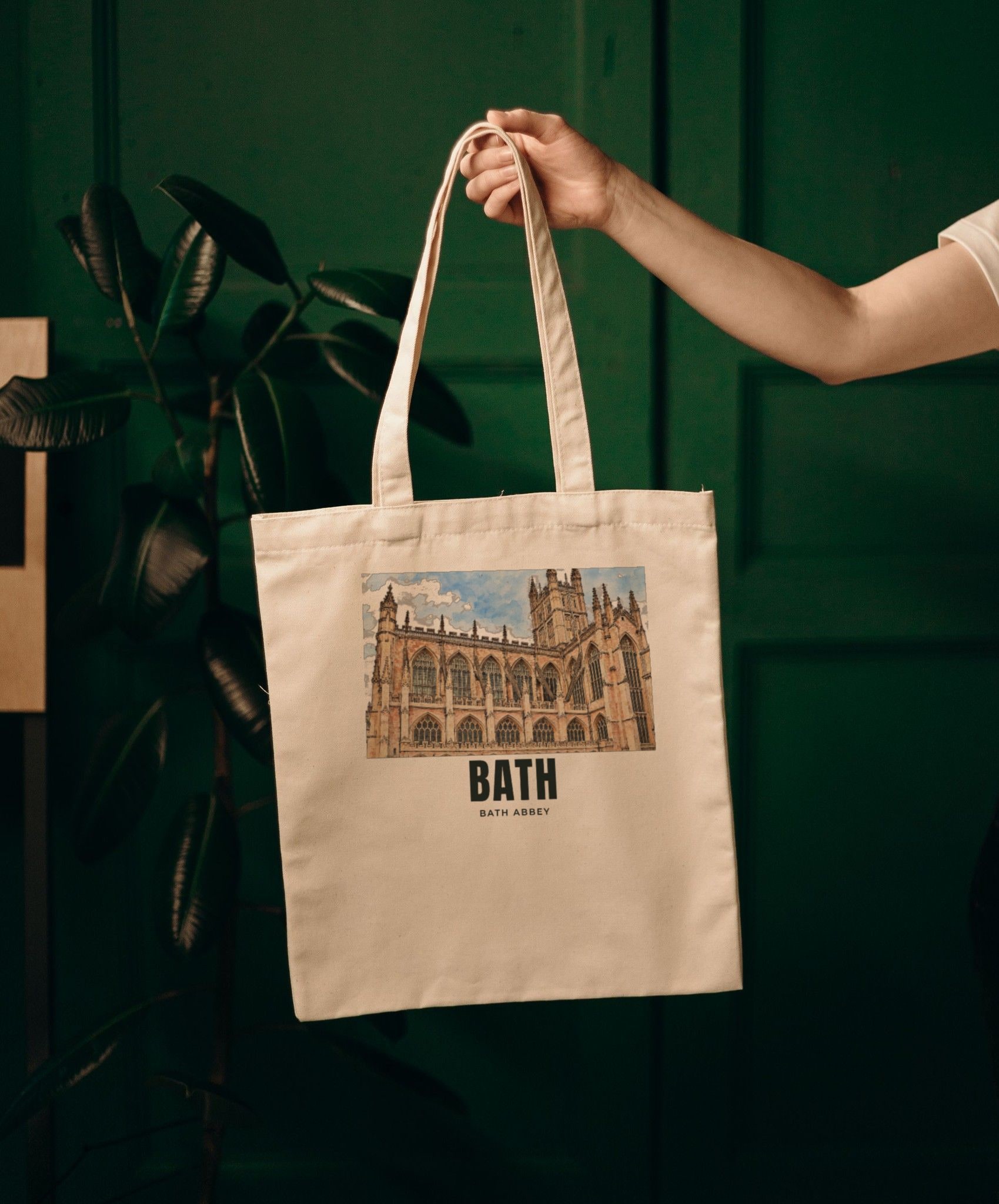 Personalised natural cotton tote bag held up, printed with a drawing of Bath Abbey and the name BATH